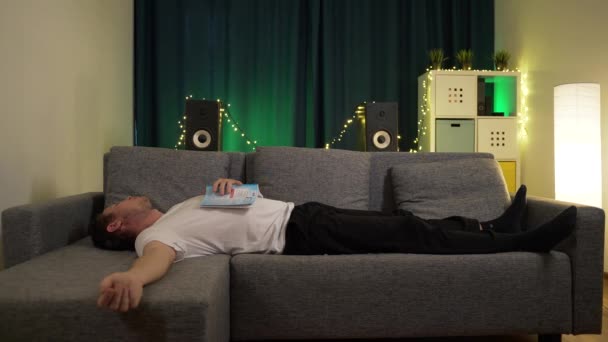 a man lies on the sofa with a book on his chest, and sleeping - Séquence, vidéo