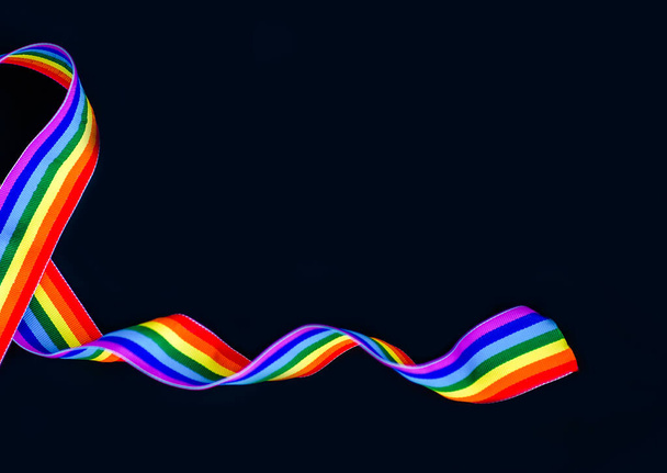 黒い背景にLGBTの虹リボン。プライドリボンシンボル。テキストのコピースペース - 写真・画像