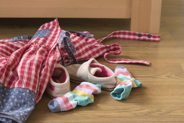 Dos calcetines y un vestido tirado en la cama. Y dos zapatillas rosas
. - Foto, imagen