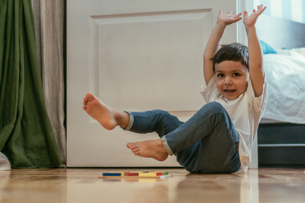selektivní zaměření roztomilé batole chlapec s rukama nad hlavou v blízkosti hraček na podlaze  - Fotografie, Obrázek