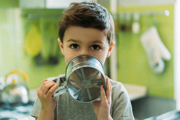 cute toddler boy covering face with baking sieve at home - Foto, afbeelding