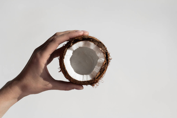 vrouwelijke hand houdt een gebroken kokosnoot op een witte achtergrond. zicht van bovenaf. - Foto, afbeelding