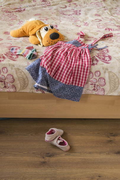 Zonnejurk en kinderspeelgoed op het bed en twee slippers. - Foto, afbeelding