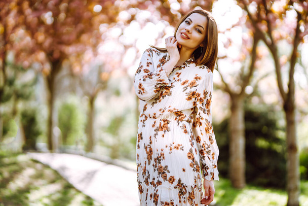 Beautiful young woman near the blooming spring tree. Attractive girl enjoying her time outside in park. Spring time. - Foto, imagen