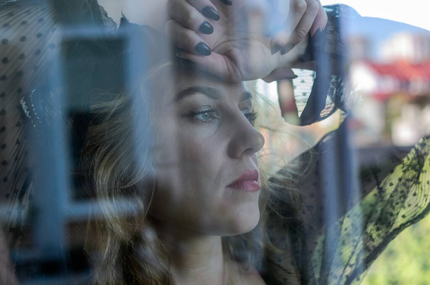 Young woman looking out of a window through a glass - Foto, Imagem