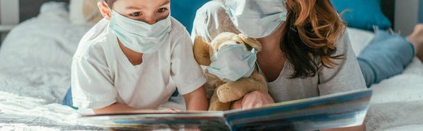 panoráma koncepció anya és kisgyermek fiú orvosi maszkok olvasókönyv közelében puha játék - Fotó, kép