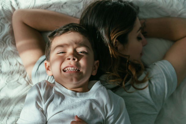 top view of toddler boy lying on back of mother in bedroom  - Foto, imagen