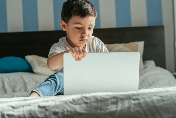 selective focus of toddler boy using laptop in bedroom  - Foto, imagen