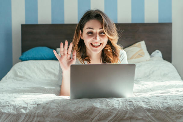 cheerful woman waving hand while having video call in bedroom  - Foto, afbeelding