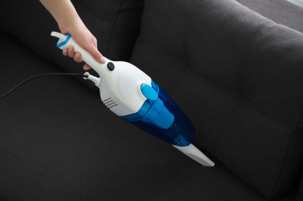 woman cleans the sofa with a hand vacuum cleaner. General cleaning of the house. Housewife is putting things in order. cleaning services - Zdjęcie, obraz