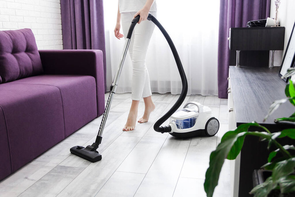 una donna in bianco sta pulendo il pavimento con un aspirapolvere. Pulizia generale della casa. La casalinga sta sistemando le cose. servizi di pulizia
 - Foto, immagini