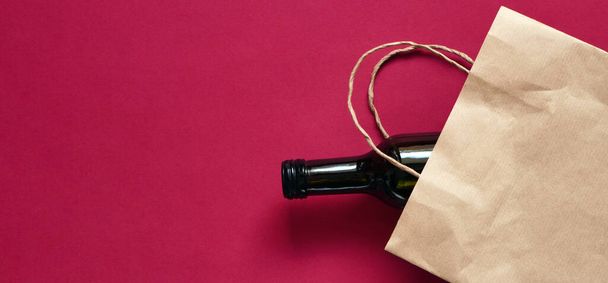 Banner paper bag with a dark glass bottle of wine, alcohol present. Flat lay on maroon background, zero waste. Garbage recycling - Photo, Image