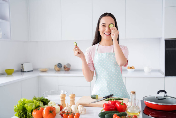 Photo of beautiful asian ethnicity housewife hold two fresh cucumber slices hiding one eye playful mood weekend cooking tasty breakfast salad stand kitchen indoors - Valokuva, kuva