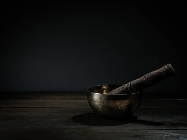 Старый тибетский чаша пения на деревянной основе, черный фон. Музыкальное лечение
. - Фото, изображение