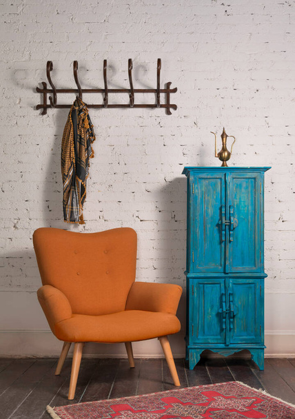 Французское оранжевое крылатое кресло, винтажный шкаф и настенная вешалка с украшенным шарфом на кирпичной стене
 - Фото, изображение