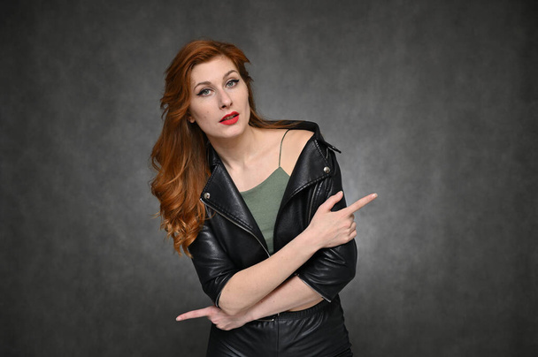 Pretty Model with great makeup posing on a gray background in the studio. Horizontal portrait of a red-haired young woman in a black jacket and green t-shirt. - Fotografie, Obrázek