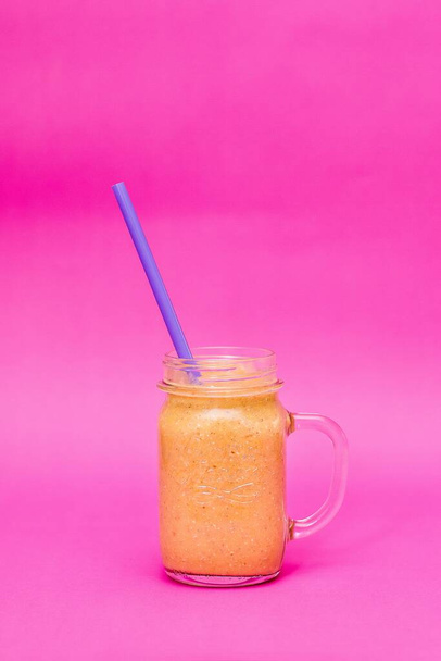 Healthy orange smoothie in a glass jar on a pink background - Φωτογραφία, εικόνα