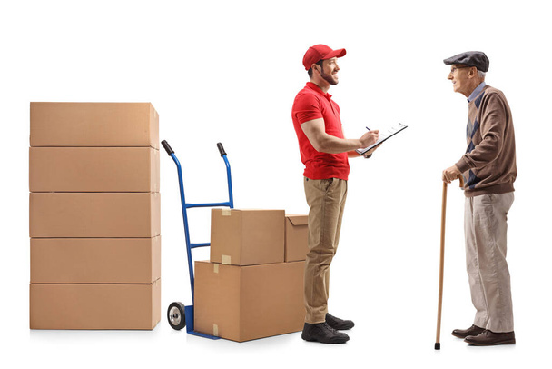 Full length shot of a delivery guy with a document handing boxes to an elderly man isolated on white background  - Valokuva, kuva