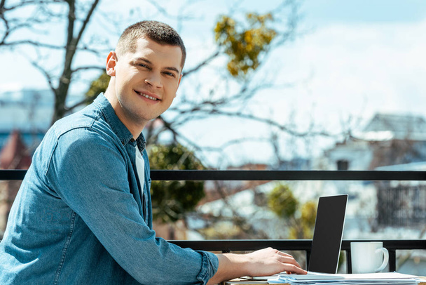smiling freelancer sitting on terrace with laptop and papers - Photo, Image
