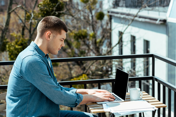 Freiberufler sitzt mit Laptop und Papieren auf der Terrasse - Foto, Bild