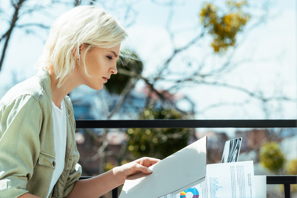 blonde businesswoman sitting on terrace with folder and papers - Photo, image