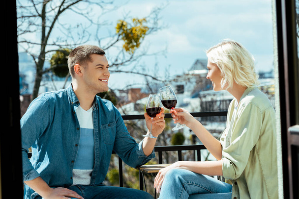 glimlachend paar kloppen met wijnglazen op zonnig terras - Foto, afbeelding