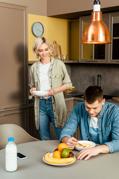pareja sonriente desayunando con cereales y frutas en la cocina
 - Foto, imagen