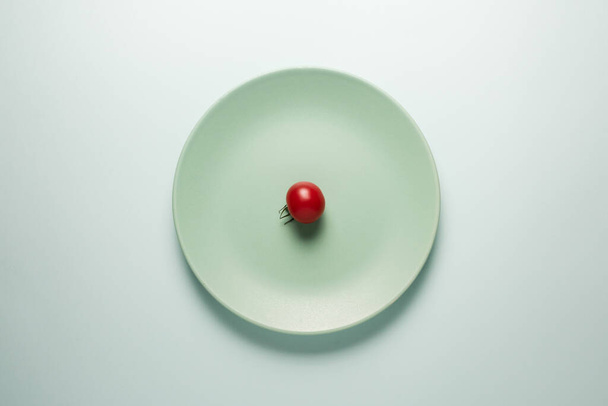 Turquoise plate with red tomato on a light background. - Zdjęcie, obraz