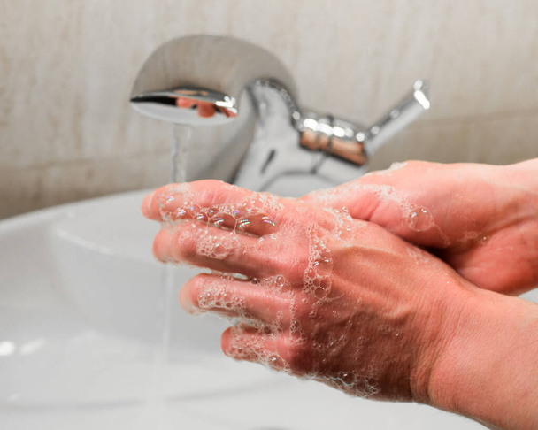 Homem lavando as mãos com água e sabão no banheiro
 - Foto, Imagem