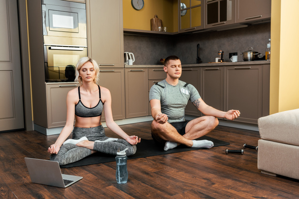 pareja joven practicando yoga en línea juntos en pose de loto en el portátil en casa durante la cuarentena
 - Foto, Imagen