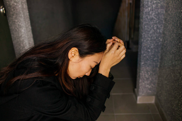 Jonge vrouw in depressie. Droevige vrouw omhelst haar knie en huilt alleen in een donkere kamer. - Foto, afbeelding