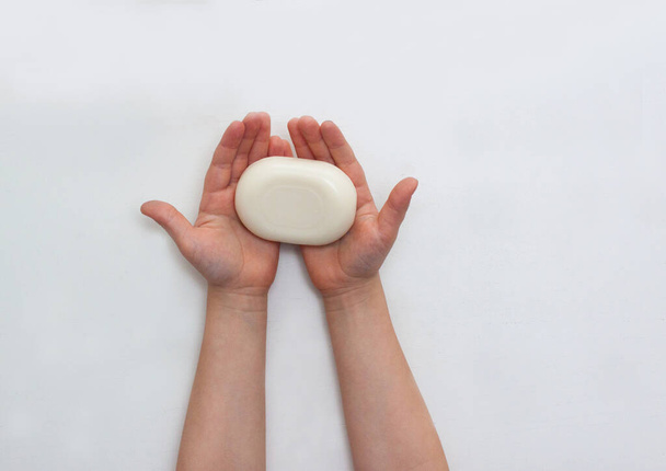 Child hands holding white soap bar above white wooden table. Illness prevention concept. - Photo, image