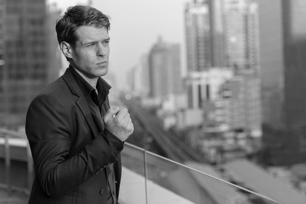 Portrait of young handsome businessman in suit against view of the city in black and white - Foto, afbeelding