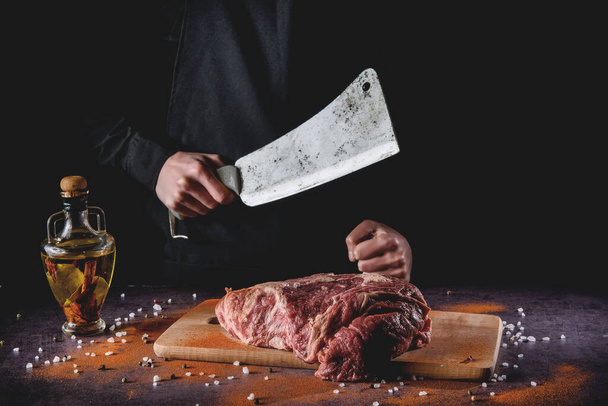 Butcher cuts fresh meat on the wood board.Beef steak and salt on background with free space for text design or logotype menu restaurant. - 写真・画像