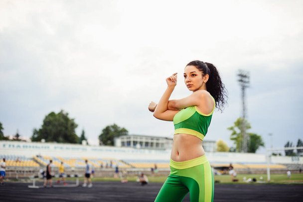 Curly-haired brunette playing sports at the stadium. Girl doing stretching, warming up hands - Fotoğraf, Görsel