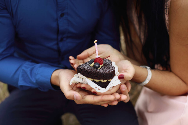Schokoladenkuchen mit Beeren und brennender Kerze für verliebtes Paar. Leckeres Dessert in Herzform für Hochzeitstag oder Geburtstagsfeier. Mann in blu und Frau in pink mit leckerem Brownie. - Foto, Bild