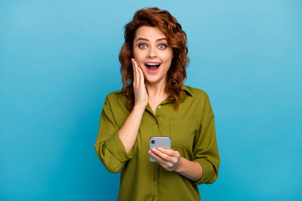 Astonished positive woman impressed she get hundred social network followers subscribers smartphone touch hand face scream wow omg wear good look clothes isolated blue color background - Fotoğraf, Görsel