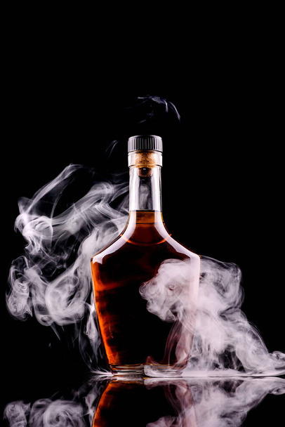 bottle and glass of whiskey or cognac with smoke on dark background - 写真・画像