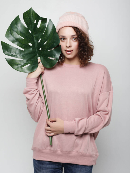Young beautiful woman wearing pink casual clothes, holding a leaf of monstera - Photo, Image