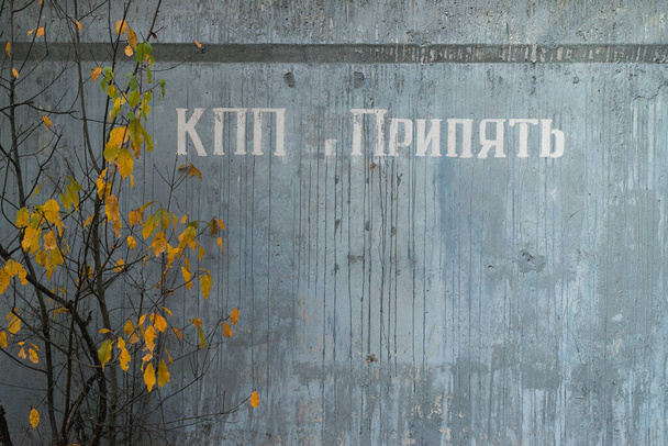 Mauer eines Checkpoints in der Nähe der Geisterstadt Pripjat, einer postapokalyptischen Stadt, Herbstsaison in der Sperrzone von Tschernobyl, Ukraine. Inschrift auf Russisch: "Checkpoint Pripjat" - Foto, Bild