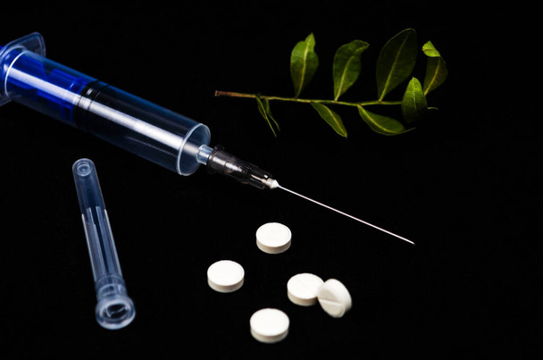 An open syringe with a cap and a bunch of white pills on a black background. The concept of the disease, addiction, treatment - Φωτογραφία, εικόνα