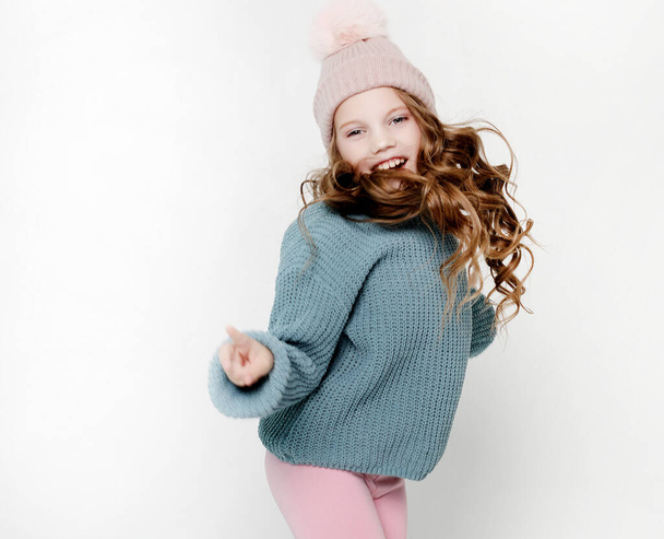 Childhood, fashion and people concept: Little girl in pink hat and blue sweater jumping on the white background. - Photo, Image