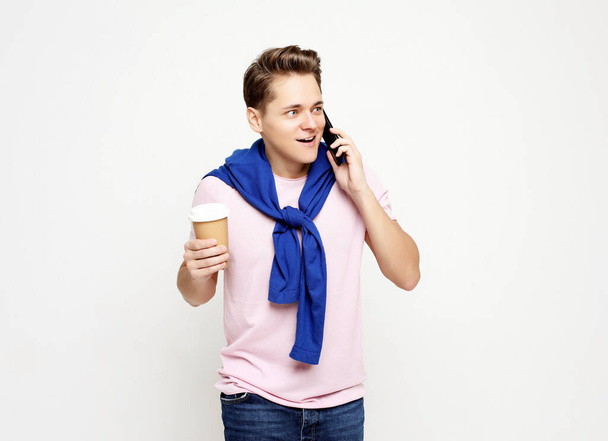 young man talking on mobile phone, drinking takeaway coffee - Photo, Image