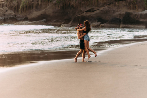 Щаслива пара йде по пляжу на заході сонця. Люблять на узбережжі. Чоловік і жінка відпочивають на морі. Гарна пара бавиться на морі. Відпустка на морі. Відпустка на острові Балі - Фото, зображення