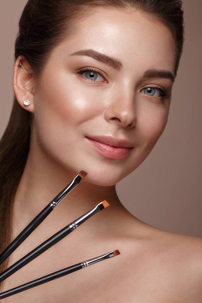 Beautiful young girl with natural nude make-up with cosmetic tools in hands. Beauty face. - Photo, Image