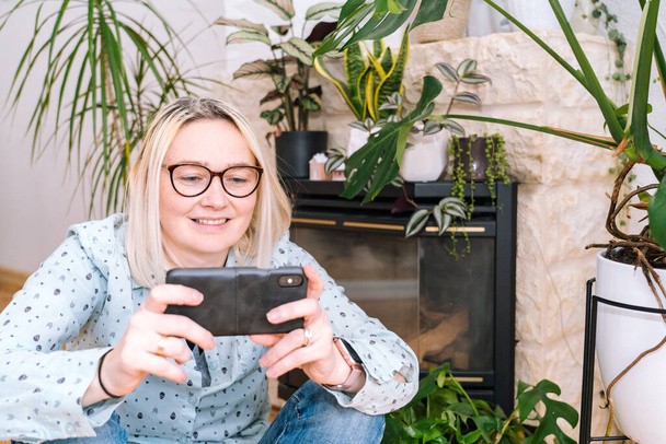 Happy girl sitting at living room and holding videocall. Young woman using smartphone for video call with friend or family. Vlogger recording webinar. Woman looking camera and waving greeting hands.  - Photo, Image