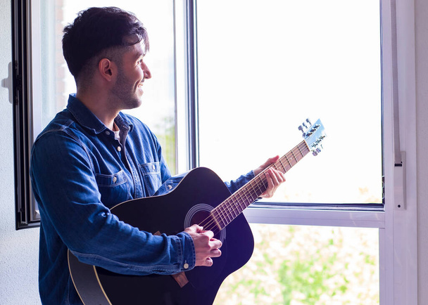 man at home by the window and plays acoustic guitar - Photo, Image