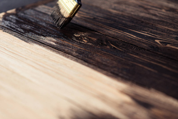 Wooden boards are half covered with stain. A brush with a wooden handle and natural bristles on a background of painted wooden planks. The painting process, the layout. - Photo, Image