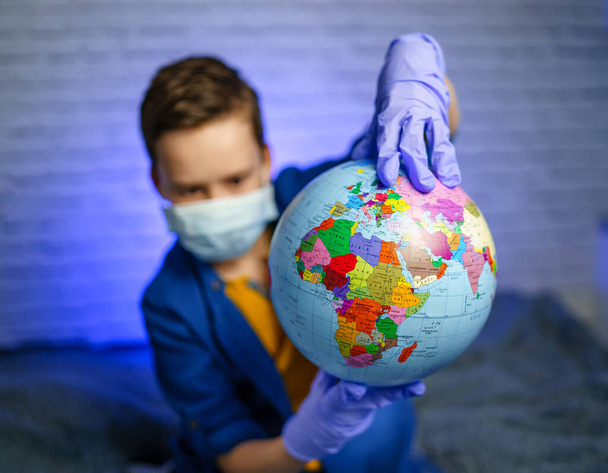 A child in a medical mask holds a globe. Little boy heals the planet. Concept of air and environment pollution. - Foto, Imagen