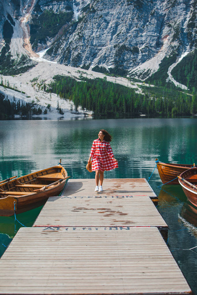 молода красива жінка в червоній сукні, що йде дерев'яним пірсом на гірському озері. літній час
 - Фото, зображення